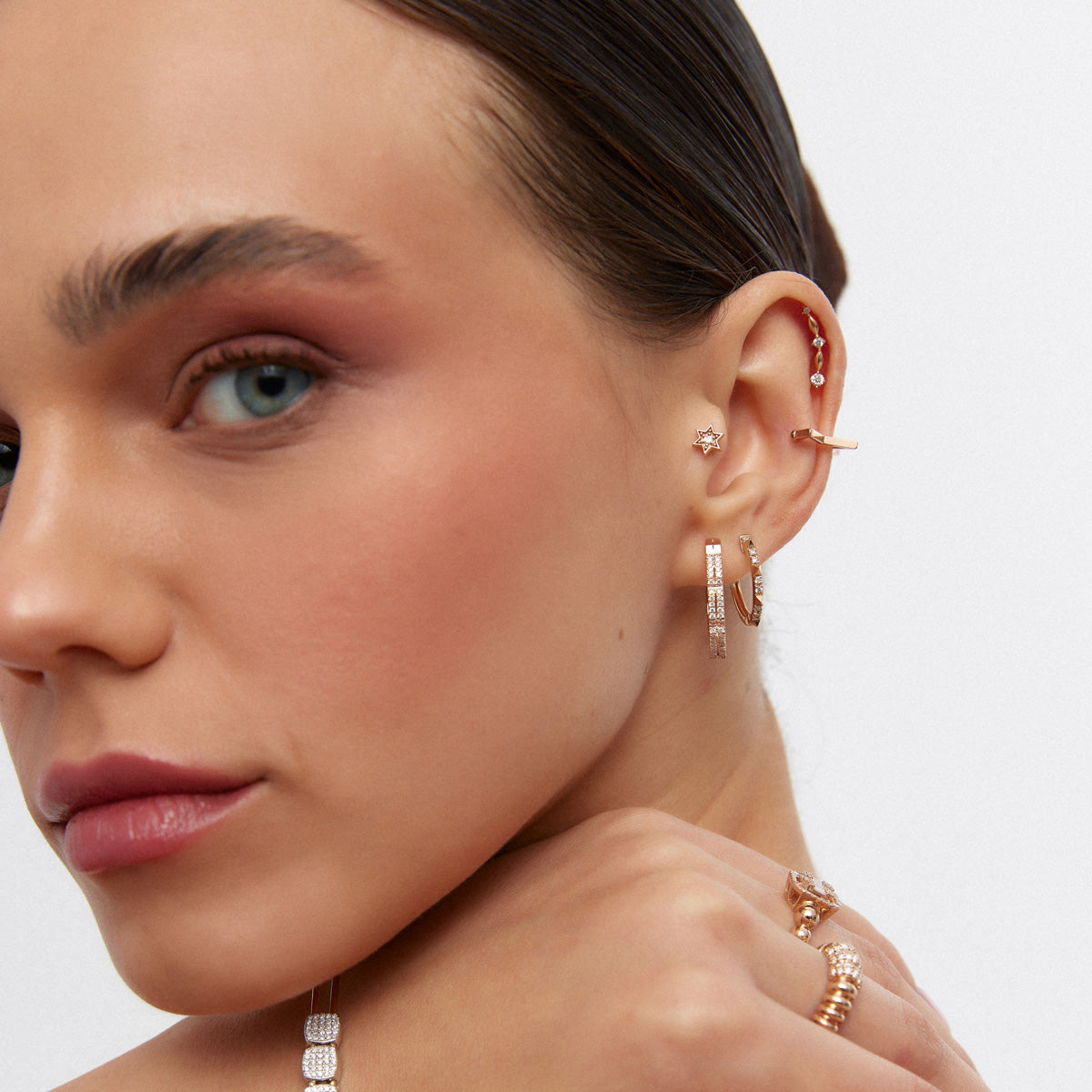 Alafine Jewelry tasarımı çoklu altın piercing ve taşlı halka küpeler, kadın modelin kulağında yakın çekim olarak sergileniyor